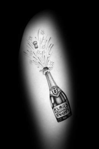 Tattoo of a champagne bottle popping with stars and bubbles, set on a light background.