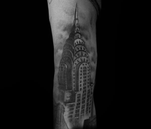 Realistic black-and-grey Chrysler Building tattoo with detailed shading and a moody sky, creating a bold architectural statement.
