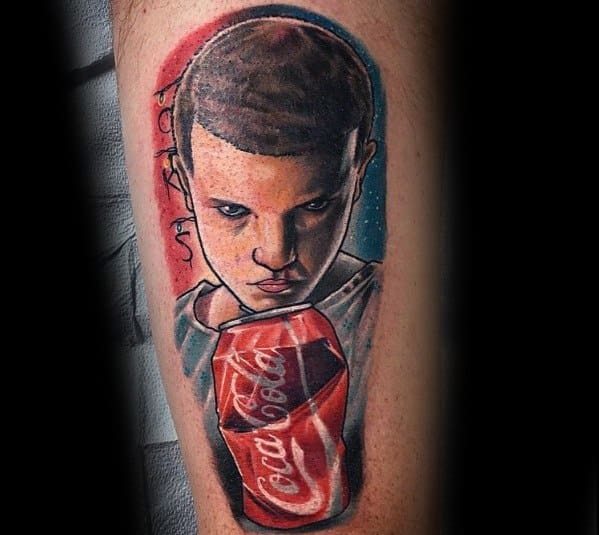 Realistic portrait tattoo featuring Eleven from *Stranger Things* holding a Coca-Cola can, with bold colors and detailed shading for a striking design.