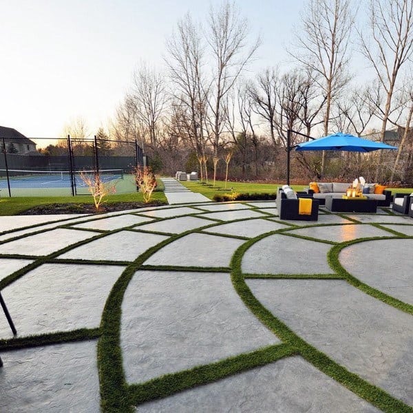 Modern backyard with tennis court, grass-filled concrete patterns, and cozy seating under a blue umbrella.