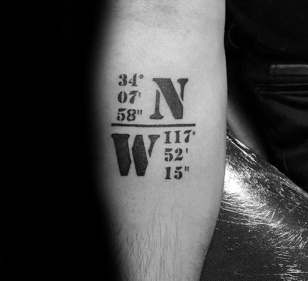 Bold coordinate tattoo on the forearm with large black lettering, featuring "N" and "W" for direction, symbolizing a significant location.