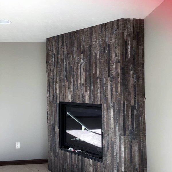 Modern corner fireplace with dark reclaimed wood paneling and a sleek black frame.