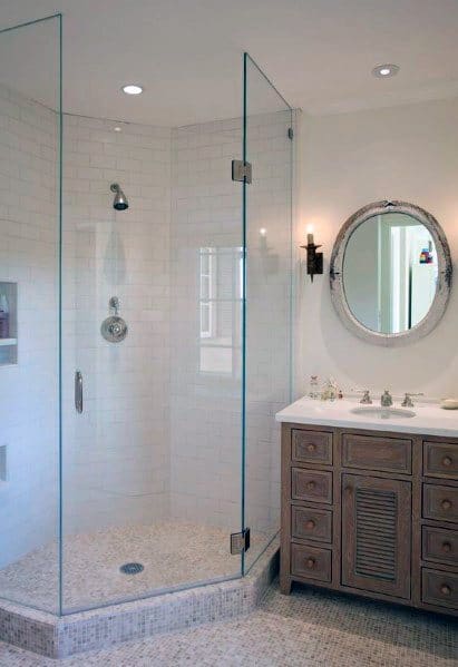 Modern bathroom with a glass corner shower, wooden vanity, round mirror, and white tiled walls