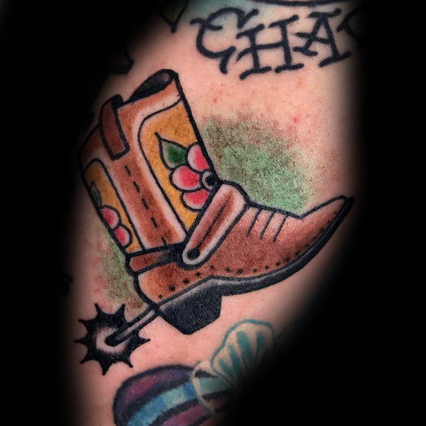 Traditional-style tattoo of a cowboy boot with floral patterns and a spur, blending Western heritage with bold, colorful design elements.