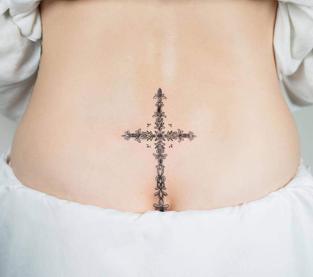 Delicate floral cross tattoo on a person's lower back