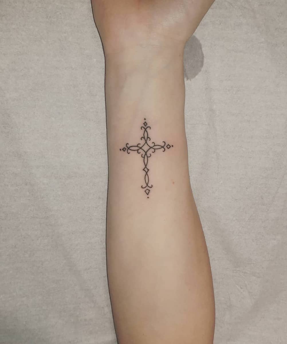 Ornate cross tattoo on inner forearm, featuring delicate lines and dots