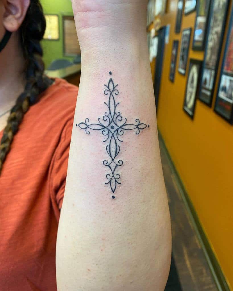 Intricate cross tattoo on forearm with elegant loops and dots