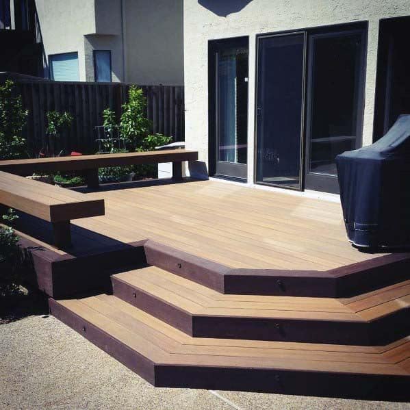 Wooden deck with stairs, a built-in bench, and grill, next to a house with expansive windows