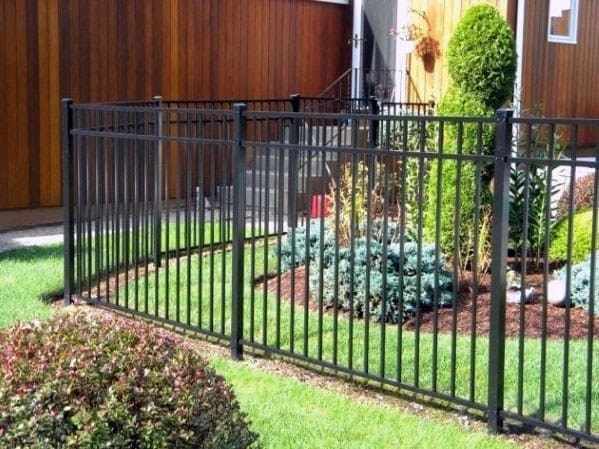 A black fence encircles a quaint garden, lush with green shrubs and plants in a cozy backyard setting