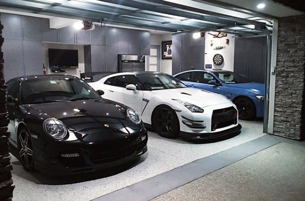 A stylish garage showcasing a Porsche, a Nissan GT-R, and a BMW, complemented by sleek cabinetry and stone accents.