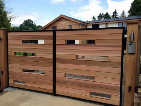 Wooden gate with horizontal slats and glass panels, in front of a modern house under a partly cloudy sky