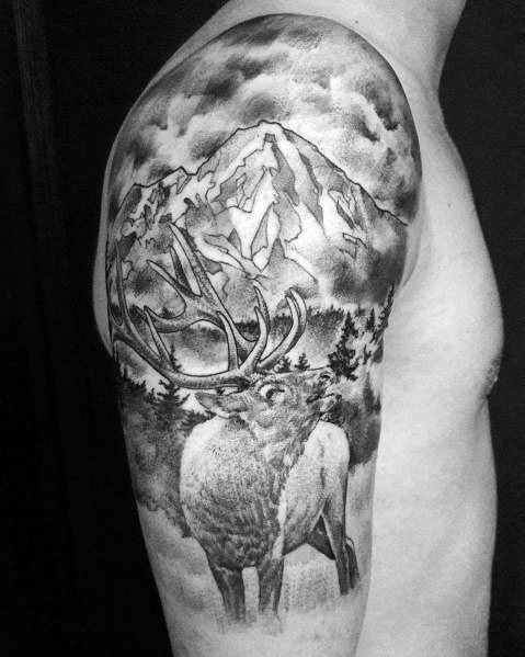 Realistic black and grey elk tattoo on the upper arm, featuring intricate shading, a mountain landscape, and forest elements for a bold nature-inspired design.