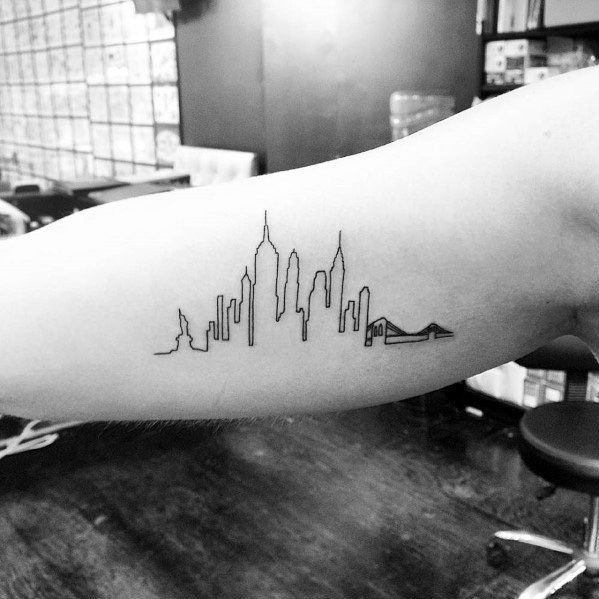 Minimalist line tattoo depicting the Empire State Building and NYC skyline, inked neatly on a man's inner bicep.