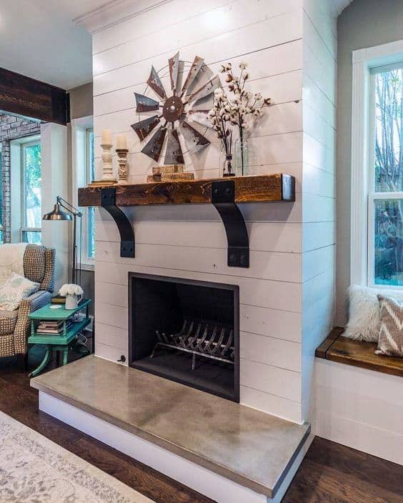 Rustic shiplap fireplace with a wooden mantel, industrial brackets, and decorative windmill art.