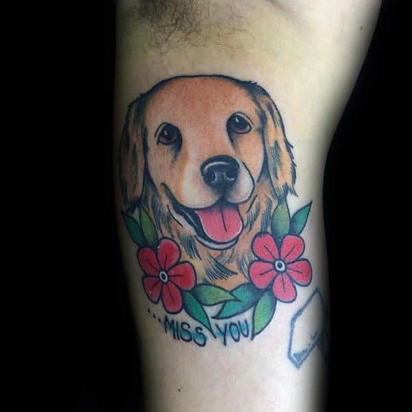 Traditional-style Golden Retriever tattoo on the arm, featuring bold outlines, vibrant colors, red flowers, and the phrase "...MISS YOU" for a heartfelt tribute.