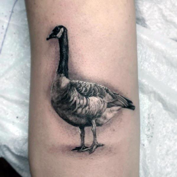 Realistic black and gray tattoo of a standing goose, inked on the forearm with fine shading and intricate feather details for a lifelike effect.