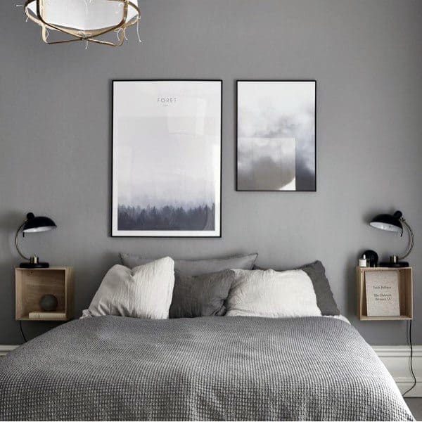 Modern bedroom with grey walls, a bed with gray and white pillows, two framed pictures, and minimalist lamps