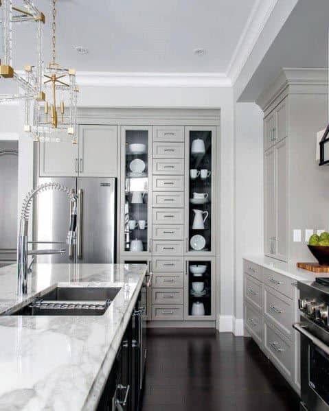 Light grey kitchen with marble countertops, glass cabinetry, and stainless steel appliances.