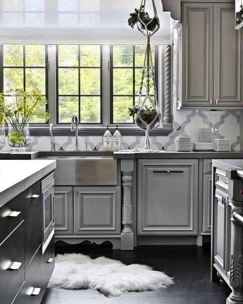 Traditional grey kitchen with ornate cabinetry, farmhouse sink, and patterned backsplash.