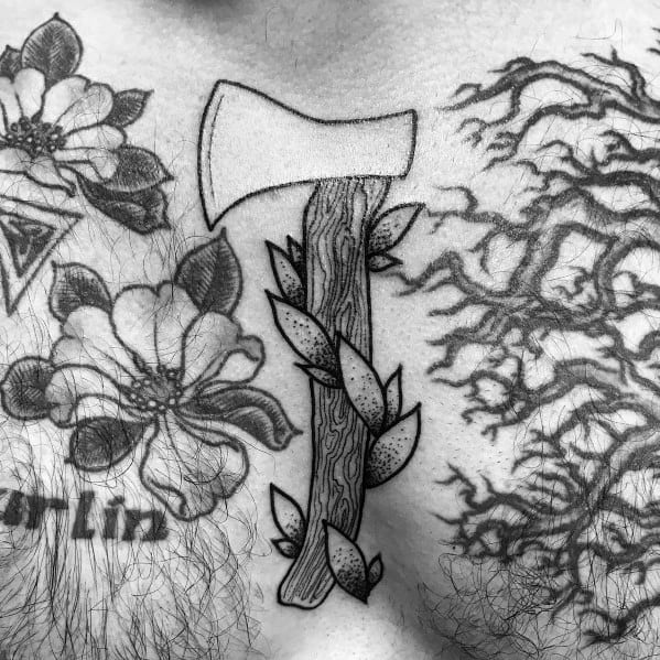 Black and gray hatchet tattoo on a man's chest, featuring a wood-textured handle with leaves, surrounded by floral and root designs.
