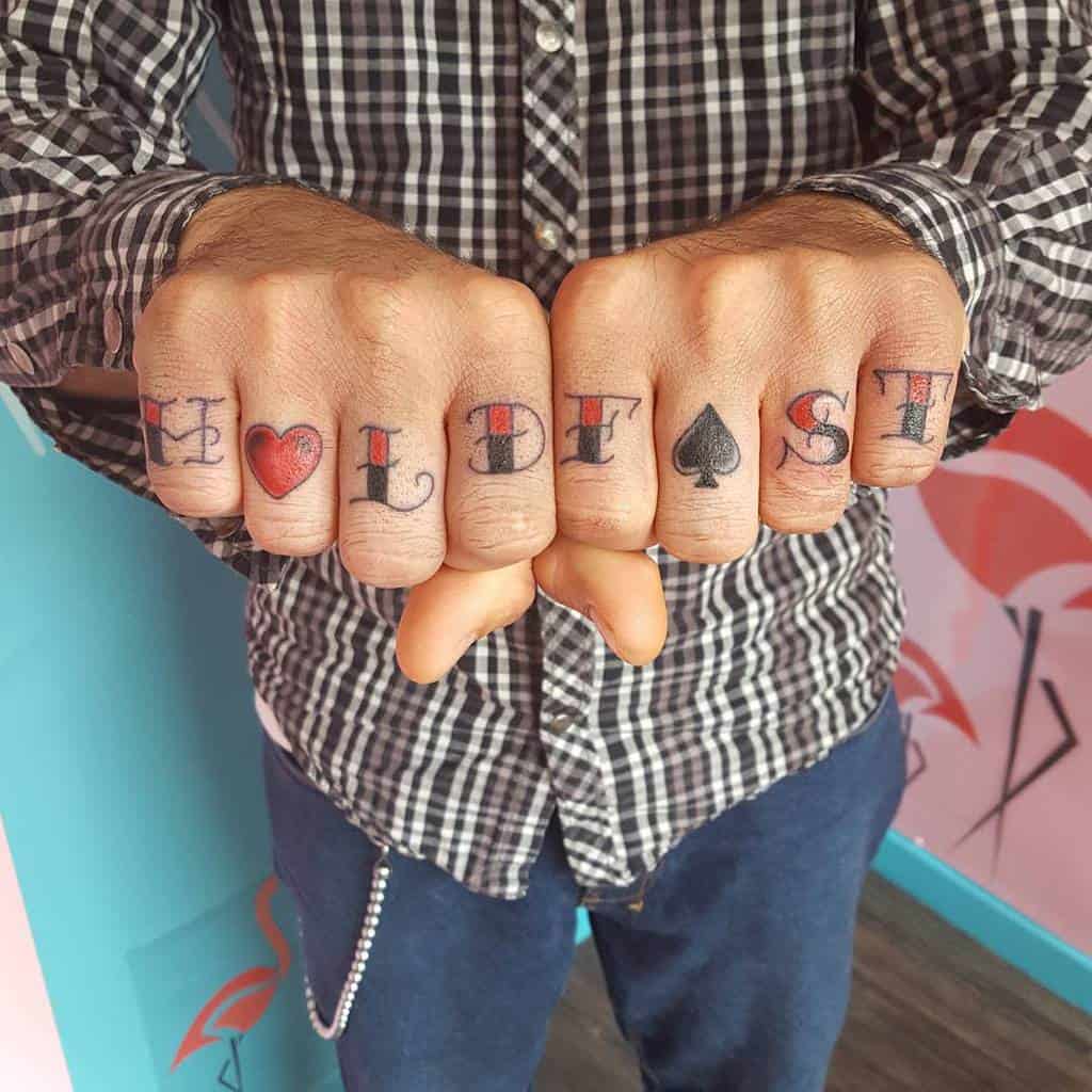 Person showing knuckle tattoos spelling "HOLD FAST" with a heart and spade symbol