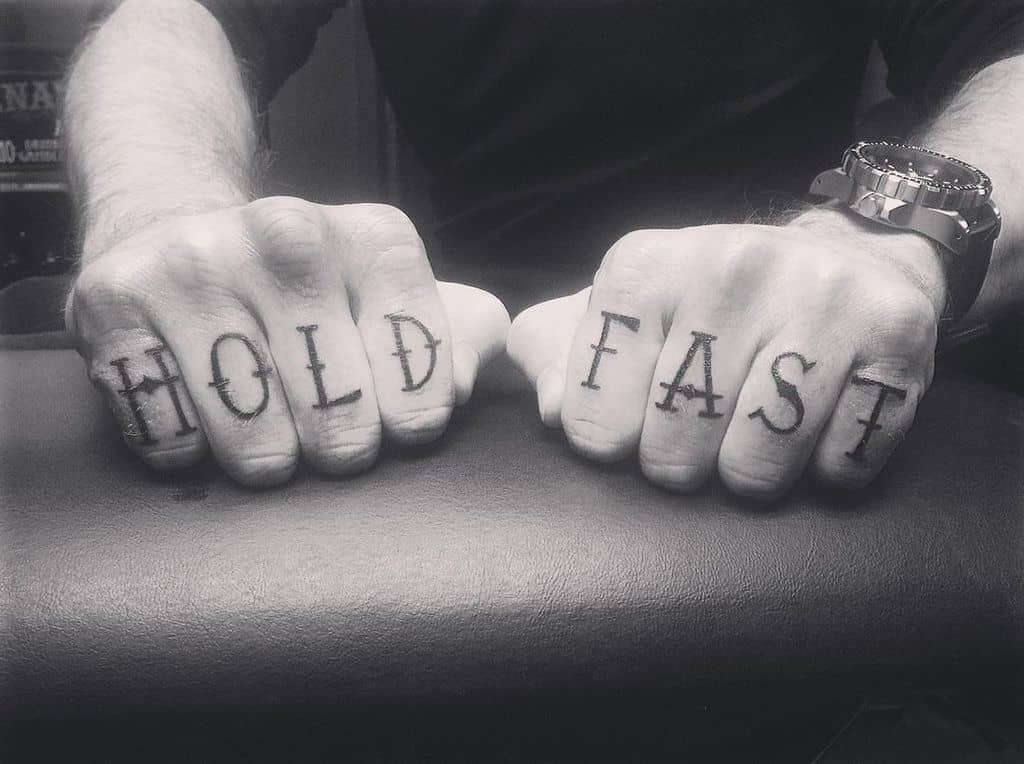 Black and white photo of tattooed knuckles reading "HOLD FAST"