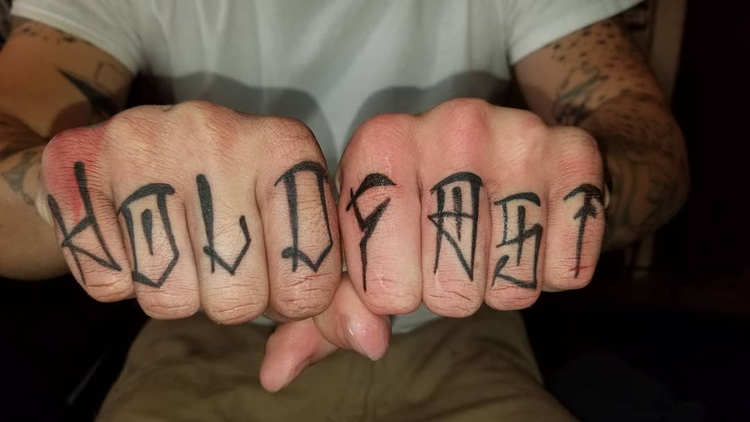 Tattooed knuckles with the words "HOLD FAST" in black ink