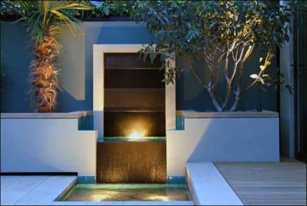 Compact wall fountain with illuminated water feature and tropical plants in a modern courtyard.