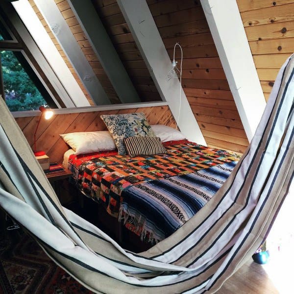 Striped hammock in a cozy attic bedroom with wooden walls and colorful bedding.