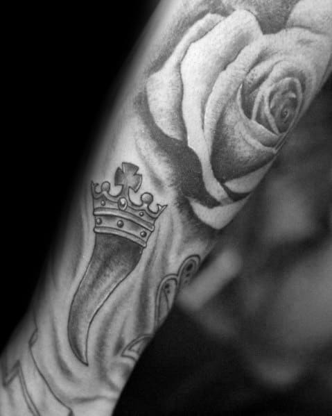 Black and grey Italian horn tattoo with a crown, placed beside a detailed rose, symbolizing protection, strength, and beauty.