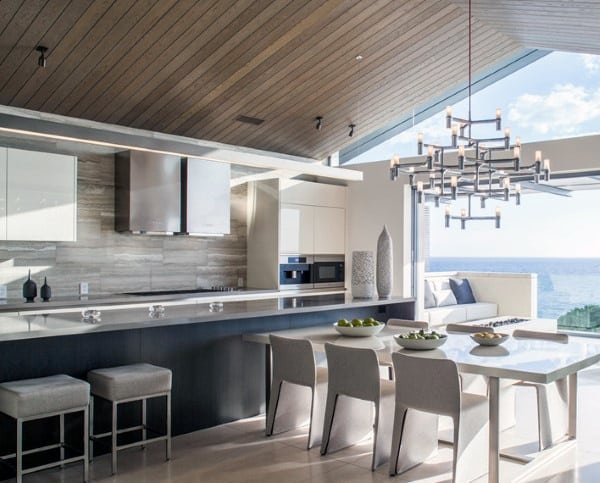 Modern kitchen with ocean view, sleek white cabinets, island, dining table, and a stylish chandelier