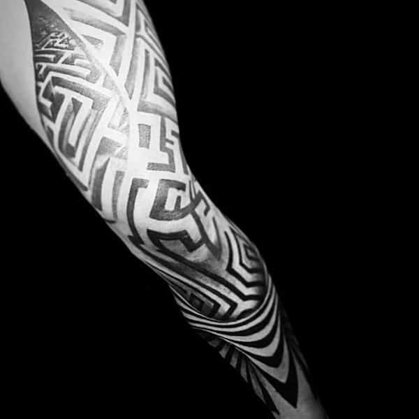 Bold blackwork labyrinth tattoo covering a man's full sleeve, featuring intricate maze-like patterns with high contrast and geometric flow.