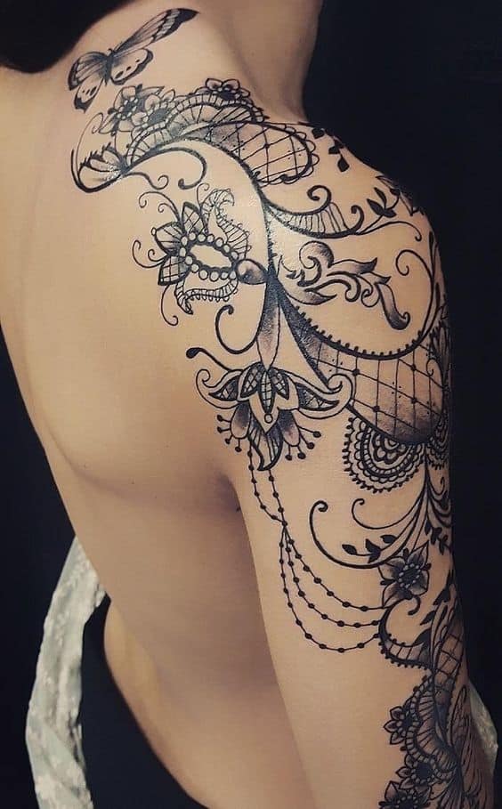 Elegant black lace tattoo flowing from the shoulder down the arm, featuring intricate floral patterns, ornamental swirls, and beaded details.