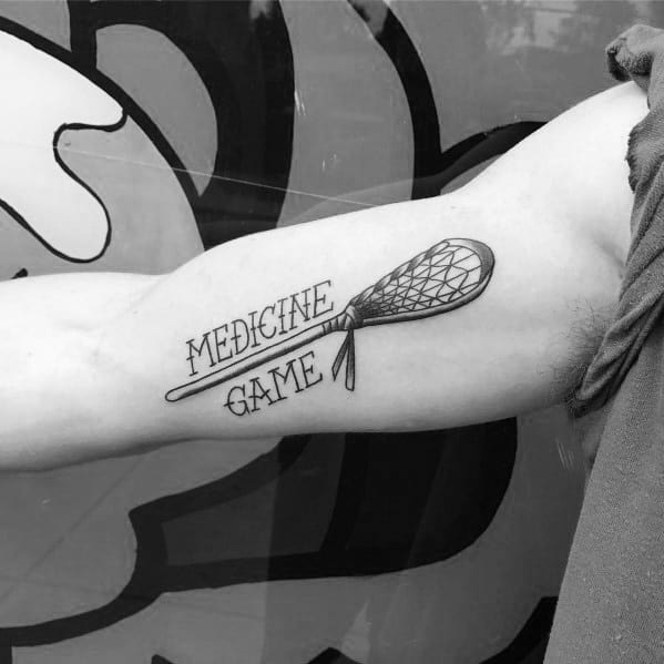 Minimalist lacrosse tattoo featuring a detailed stick with the words "Medicine Game," honoring the sport’s deep Native American roots and traditions.