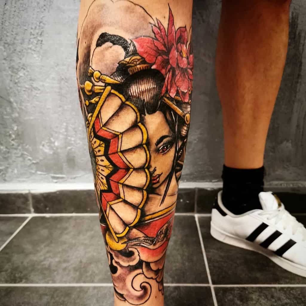 Vibrant Japanese-style leg tattoo of a Geisha partially hiding behind a detailed red and gold fan, adorned with floral accents and swirling clouds.