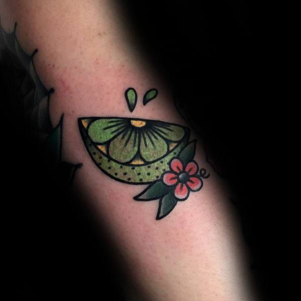 Traditional-style lime wedge tattoo with bold outlines, juice droplets, and floral accents, creating a fresh and vibrant citrus-inspired design.