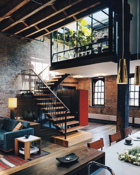 Industrial-style loft with exposed brick walls, a floating staircase, and a glass-enclosed greenery-filled mezzanine.