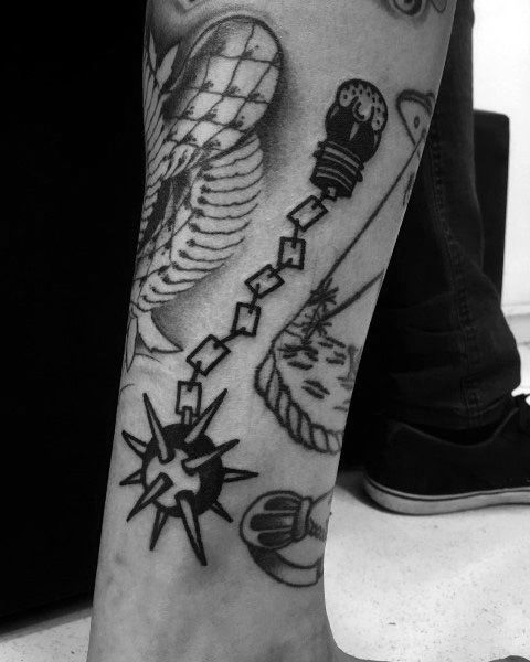 Black and gray tattoo featuring a spiked mace on a chain, surrounded by abstract and traditional elements on a person’s leg.