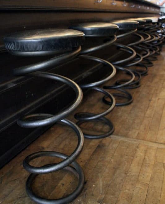 Bar stool seats designed like metal springs with black cushions lined up along a wooden floor
