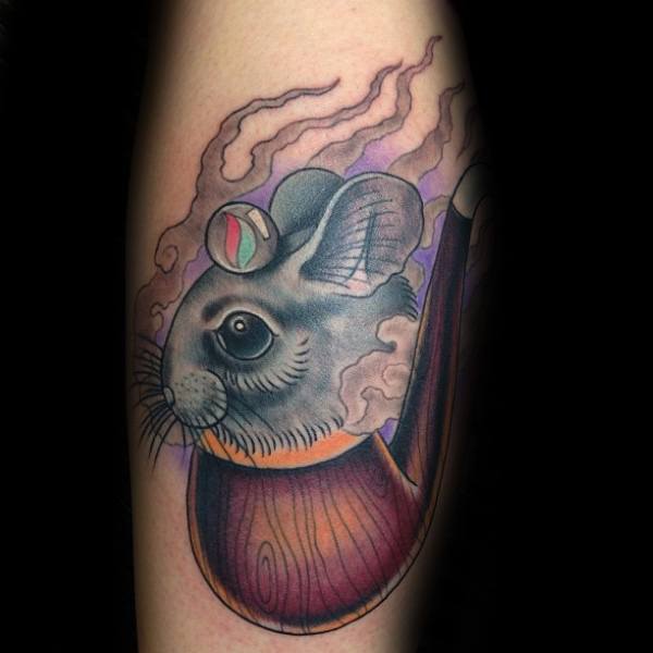 Unique tattoo of a gray mouse emerging from a wooden pipe with smoke, featuring a marble on its head, blending realism and surrealism in bold colors.
