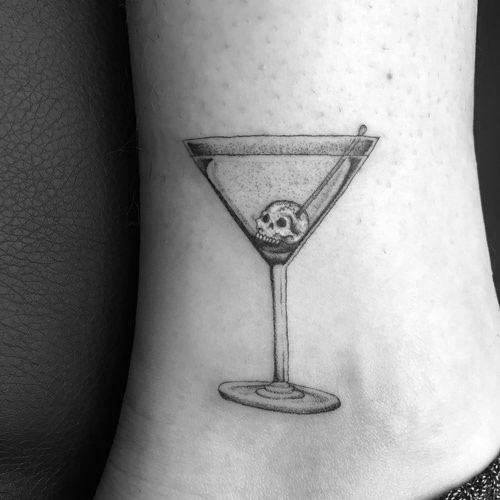 Minimalist black and grey martini glass tattoo with a tiny skull as a garnish. A sleek and edgy design with fine line details.