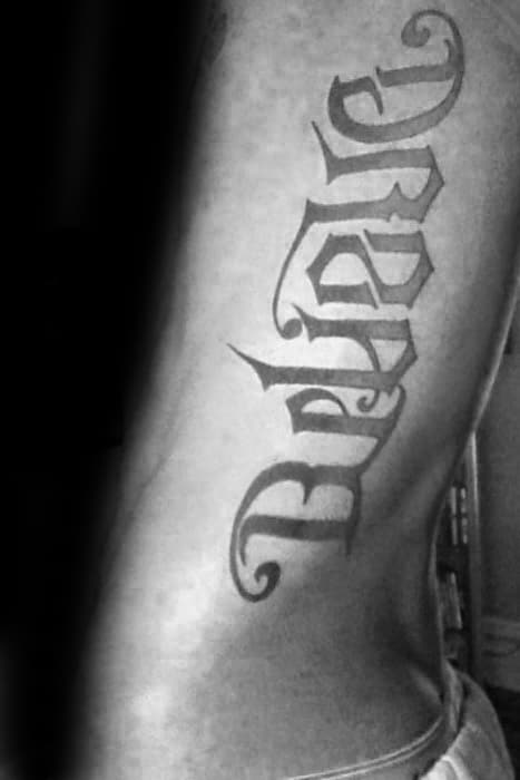 Side rib tattoo with the word “Dream” in vertical gothic lettering, featuring sharp edges and a bold, medieval-inspired design.