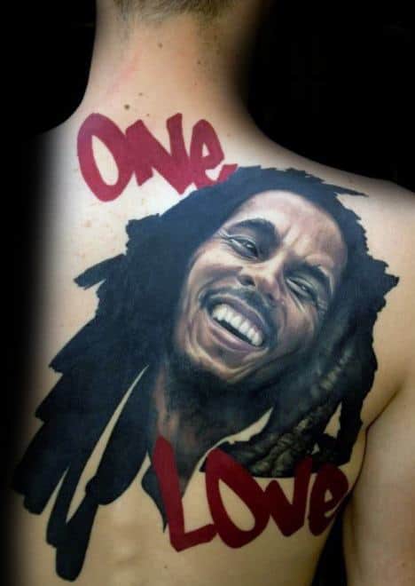 Large back tattoo of Bob Marley smiling, with bold red graffiti-style text reading "One Love" framing the portrait in a lively and expressive design.