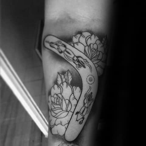Black and grey boomerang tattoo featuring Aboriginal-inspired elements and floral outlines, placed on the inner arm.