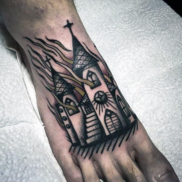Stylized burning church tattoo on the foot with tall steeples, glowing windows, and flowing flames. Black lines and muted tones create a bold look.