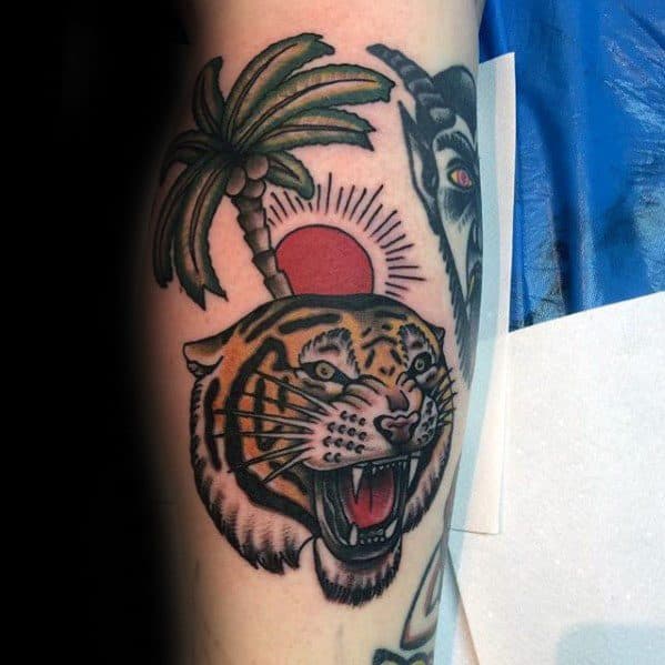 Traditional-style tattoo of a roaring tiger head with a coconut palm tree and red sunburst in the background, inked on the upper arm.