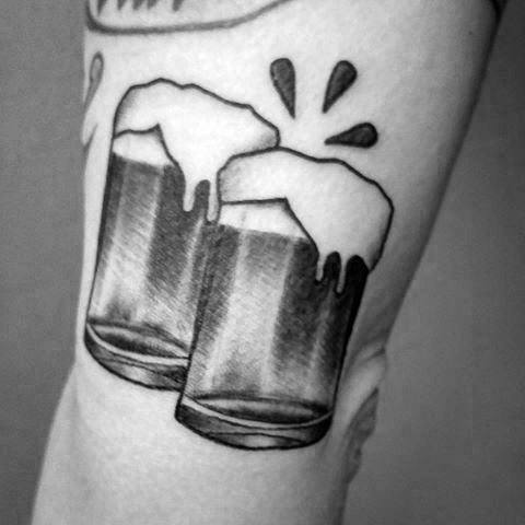 Tattoo of two foamy beer mugs clinking with an emoji vibe on an arm