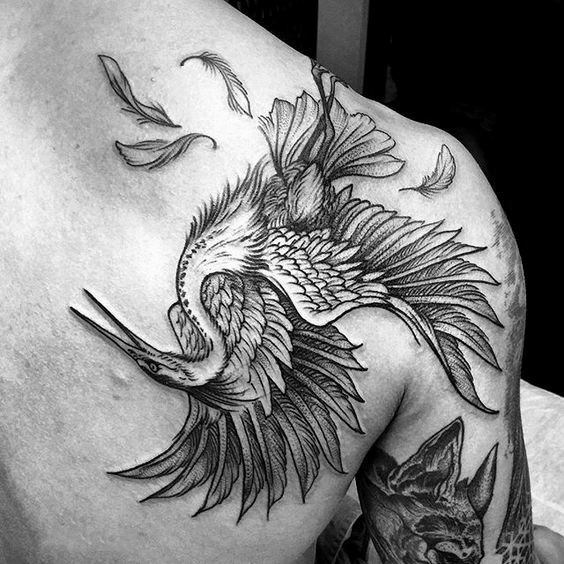 Detailed blackwork tattoo of a falling bird with scattered feathers, inked across the shoulder and upper back.
