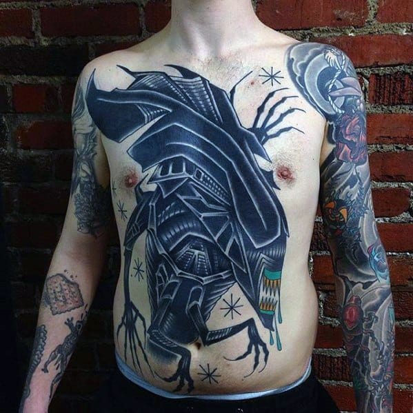 Large abstract Xenomorph tattoo across the chest and stomach with bold black shapes, tribal elements, and stylized alien features.