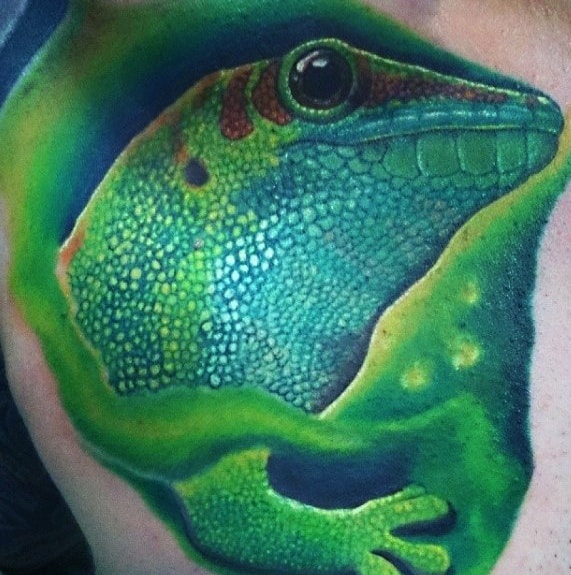 Hyper-realistic green gecko tattoo with vivid scale details, bright highlights, and a 3D effect of the lizard emerging from the skin.